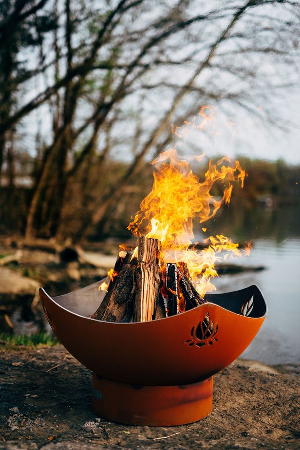 Woman meditating beside Firepit Art bowl with blazing fire at dusk